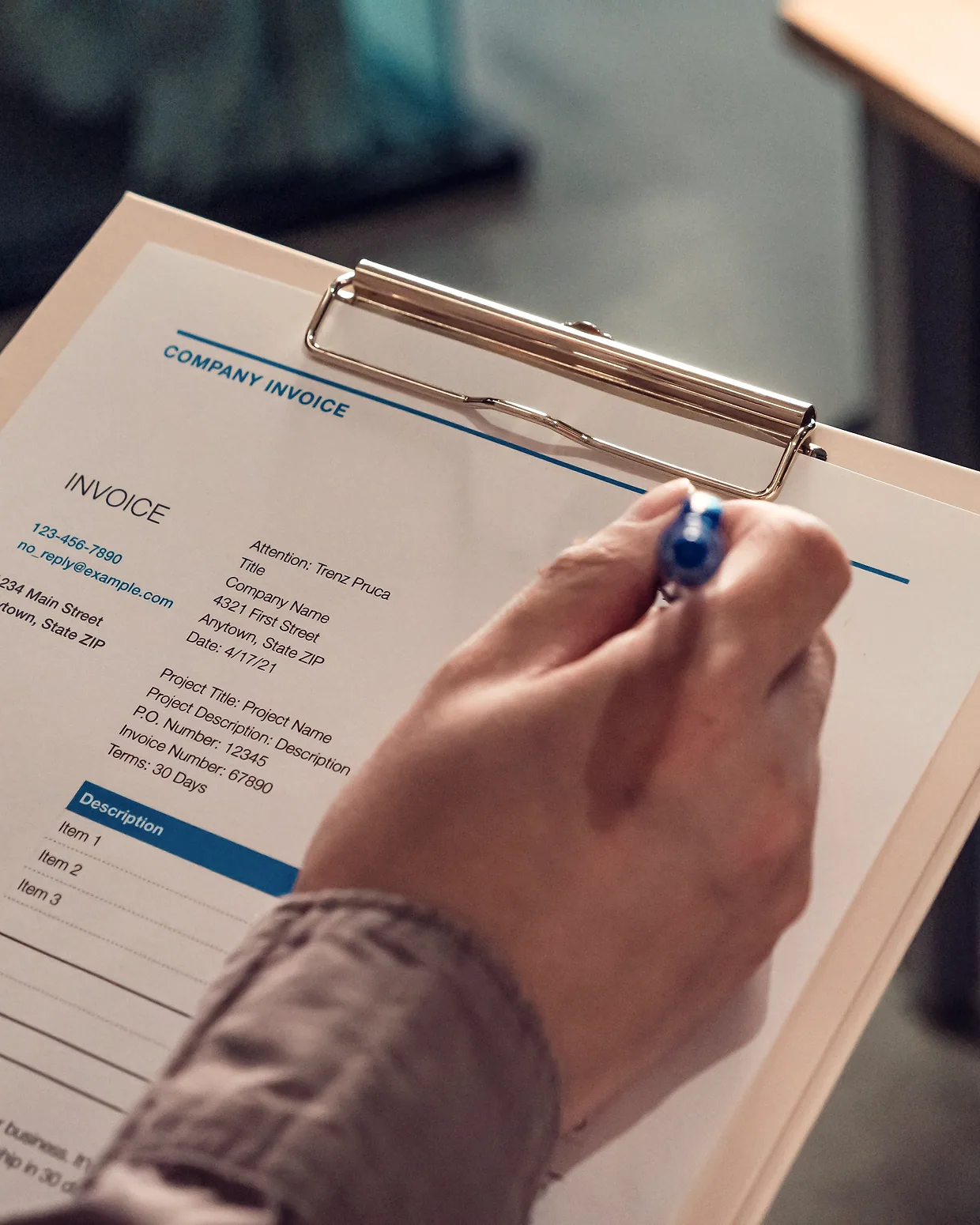 A hand filling in an invoice on a clipboard.