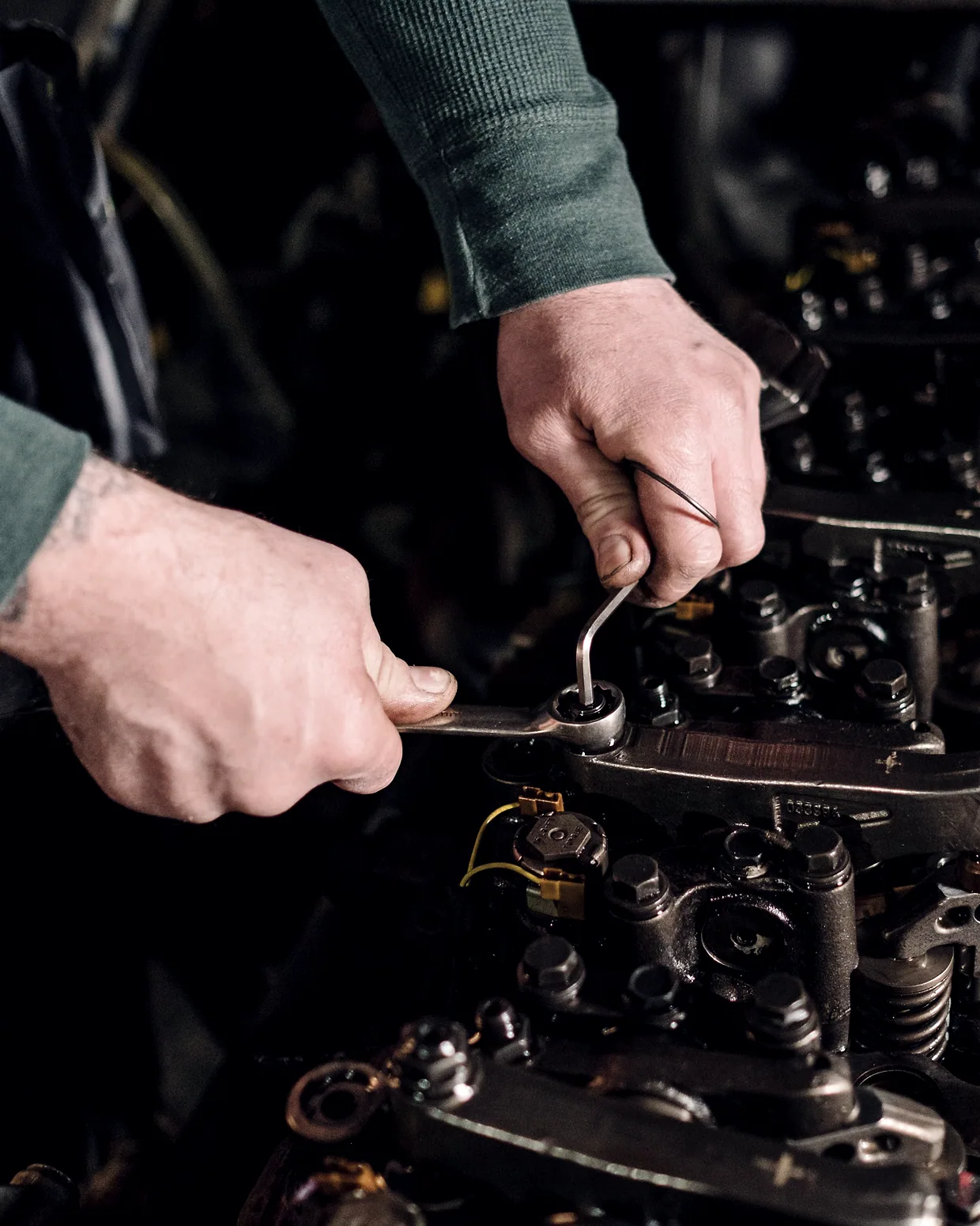 Two hands using a wrench on an exposed cylinder head.