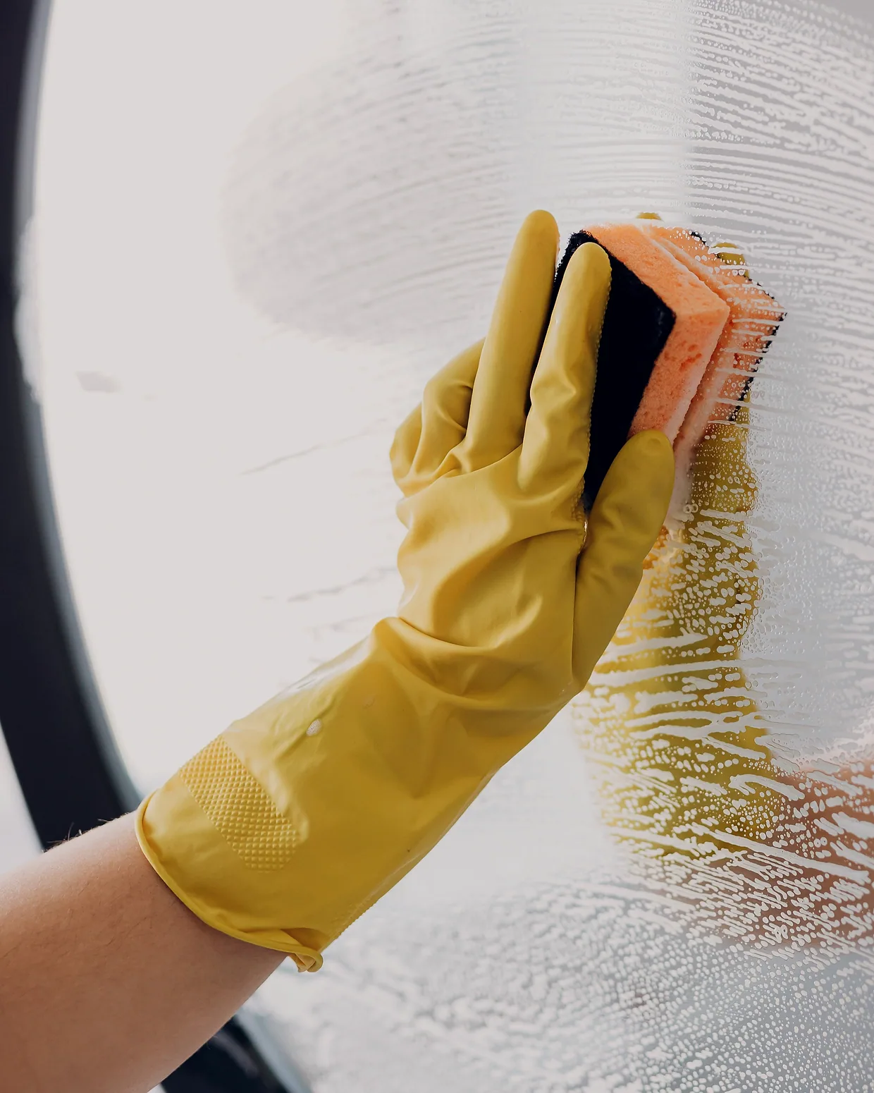 A gloved hand working a sponge across a misted mirror.