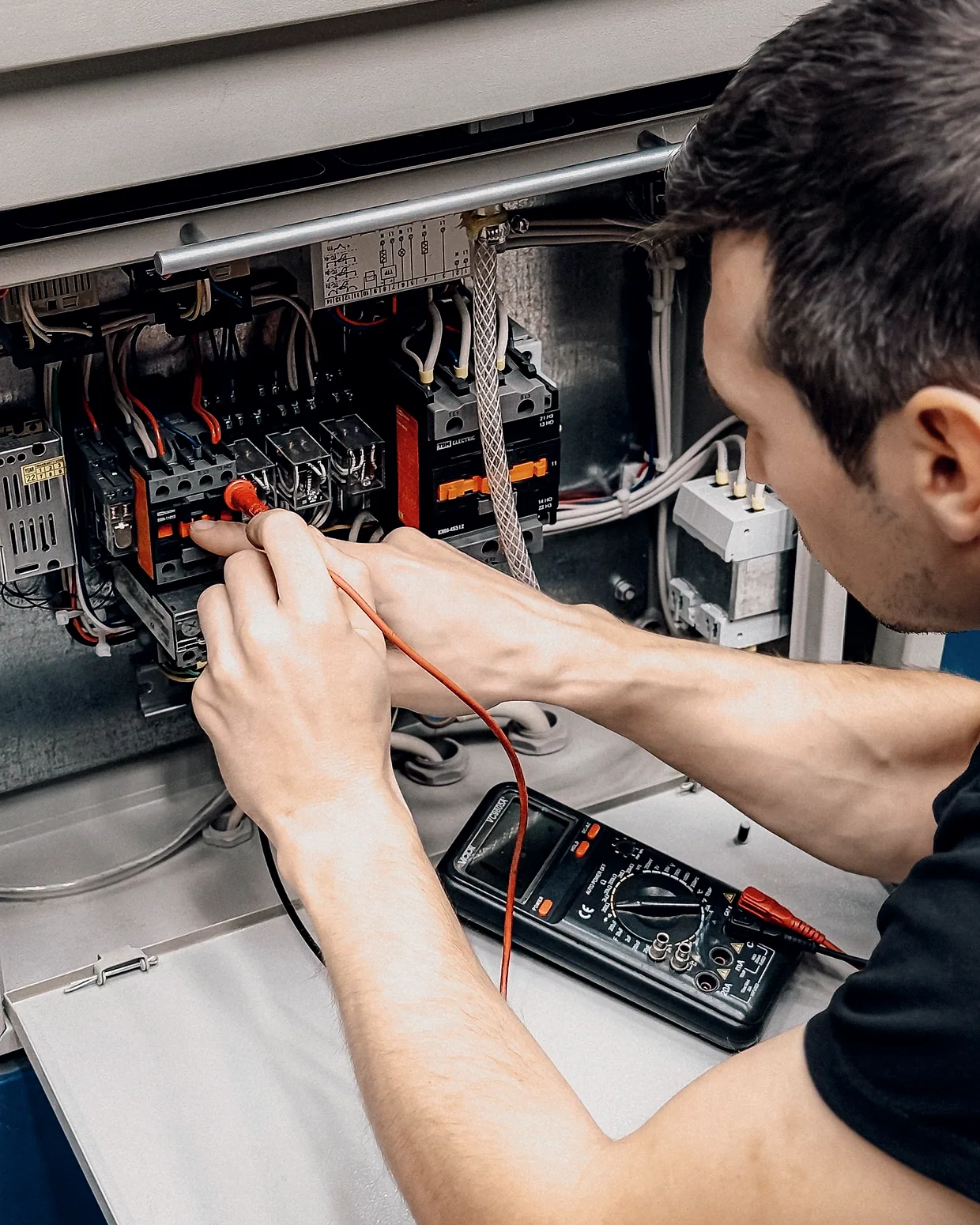 An electrician testing terminals in a panel with a multimeter.