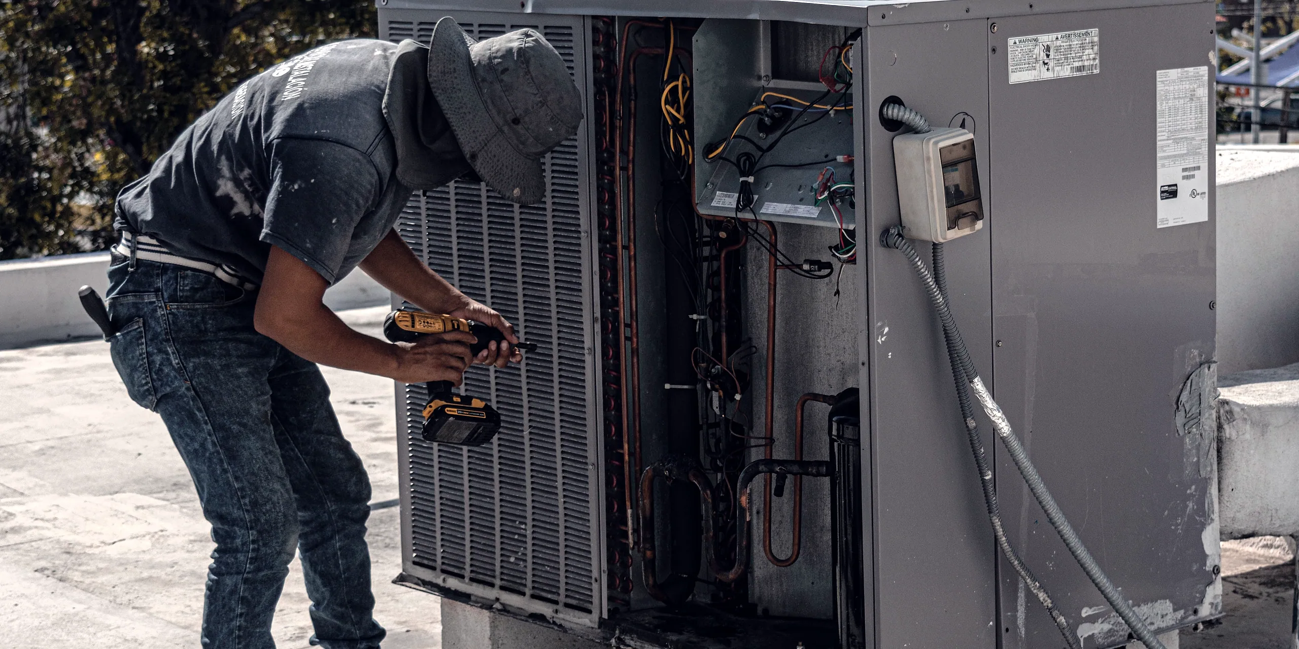 An HVAC technician bent over an outdoor condensing unit on a flat roof.