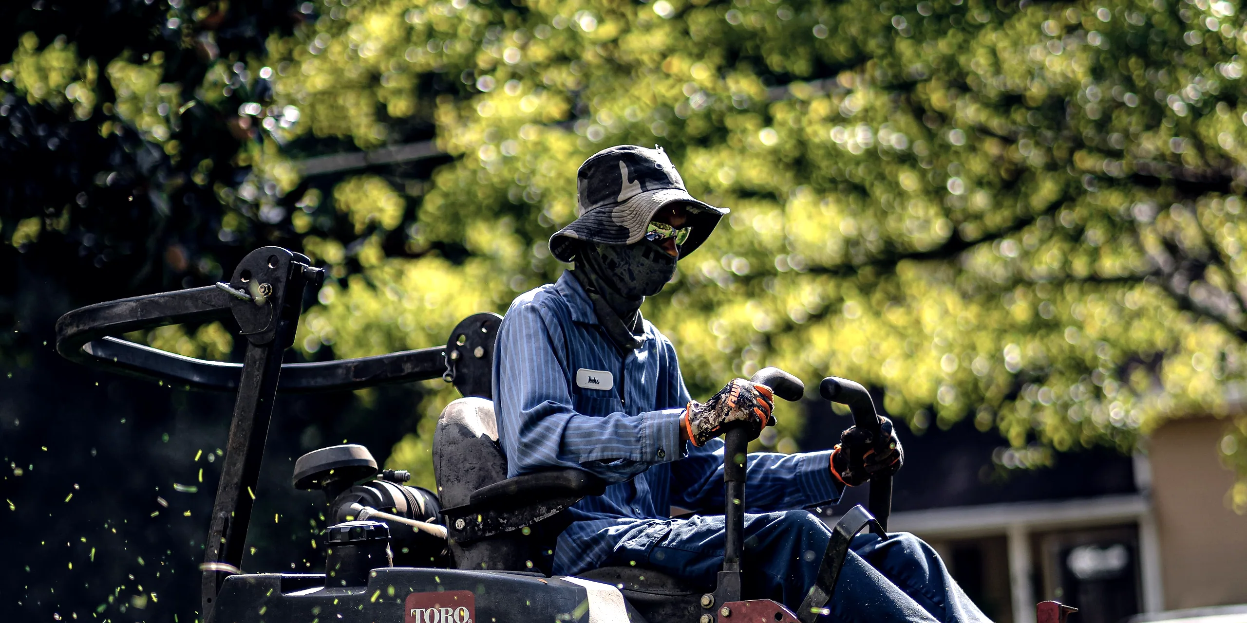 An operator on a zero-turn mower with cut grass flying behind the deck.